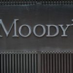 in primo piano sfocati due persone che passano di fronte l'insegna, in secondo piano, di moody's